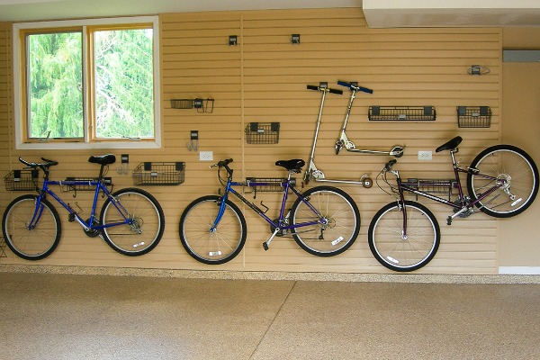 Several bikes and gear are stored on this slatwall panel in oak color. 